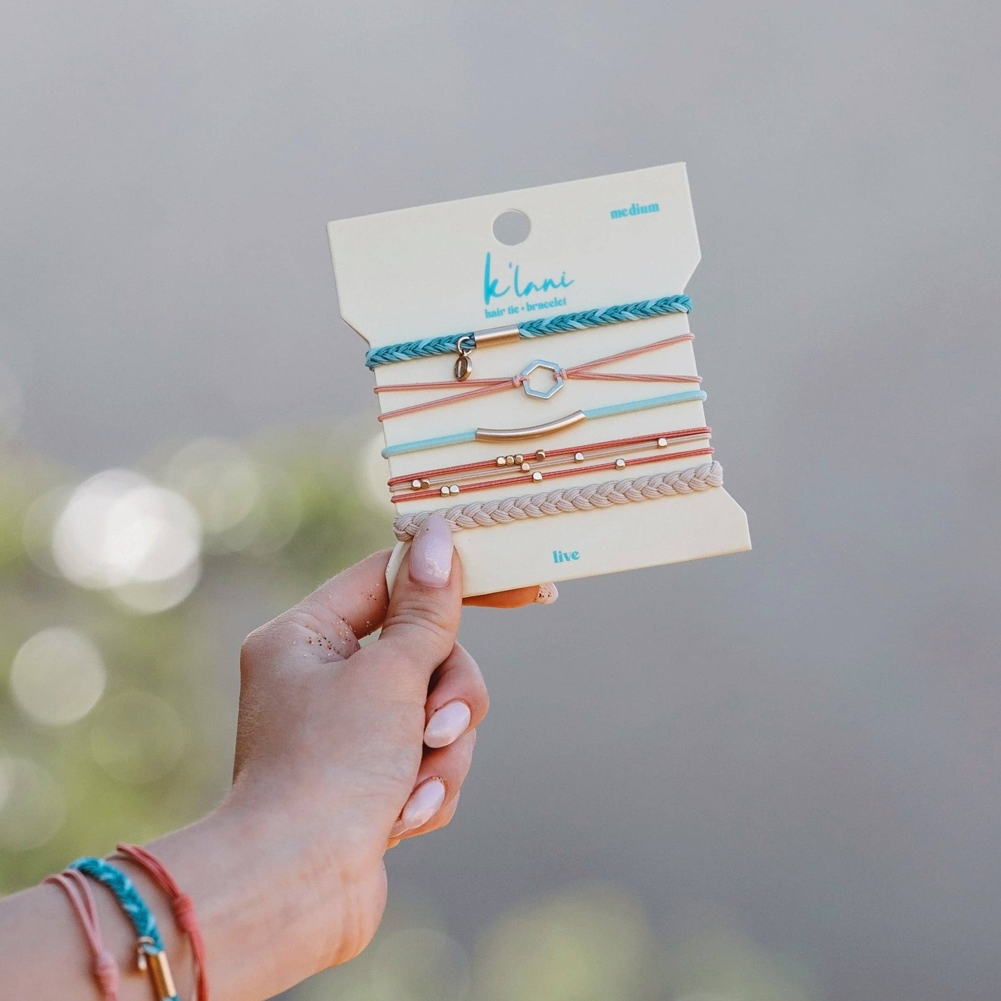 Hand holding a package of colorful bracelets with 'kibrace' branding against a blurred natural background.
